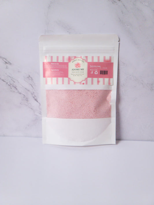Pink bath soak packaged in a white pouch.
Text: Merci Belles Adore Me Fizz Bath Soak. Handmade with love. 5oz.